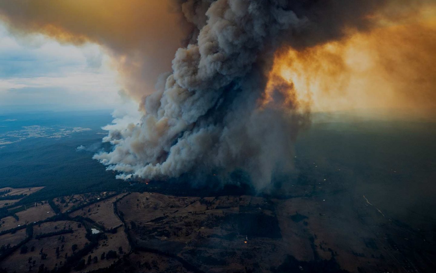 Aerial view of a dark smoke plume rising high above a forest and rural landscape.
