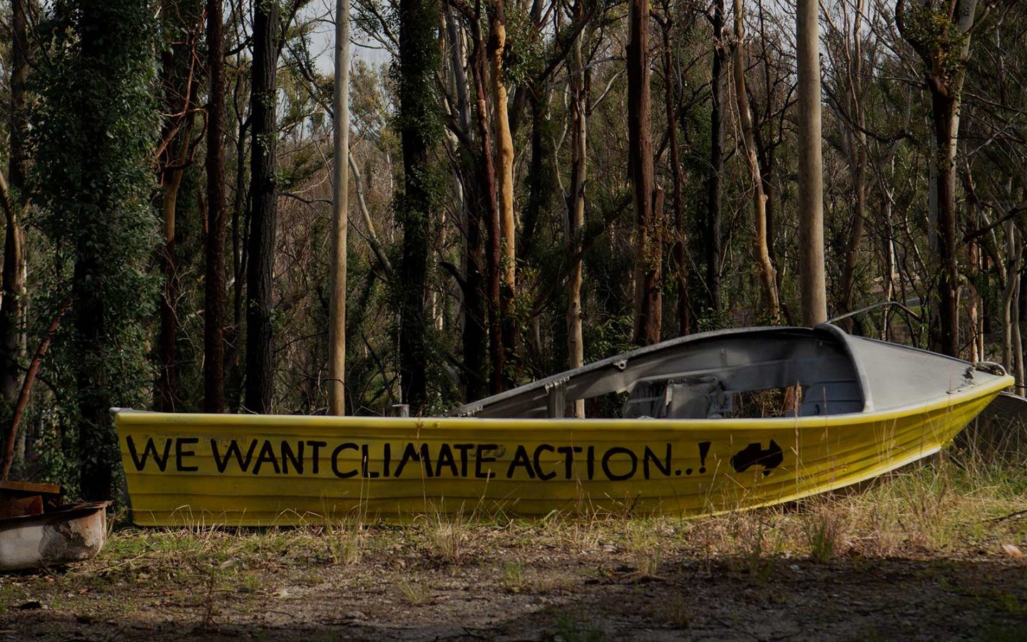 An aluminium boat on land in front of a forest of small trees, with the words 'We want climate action' painted beside a map of Australia.