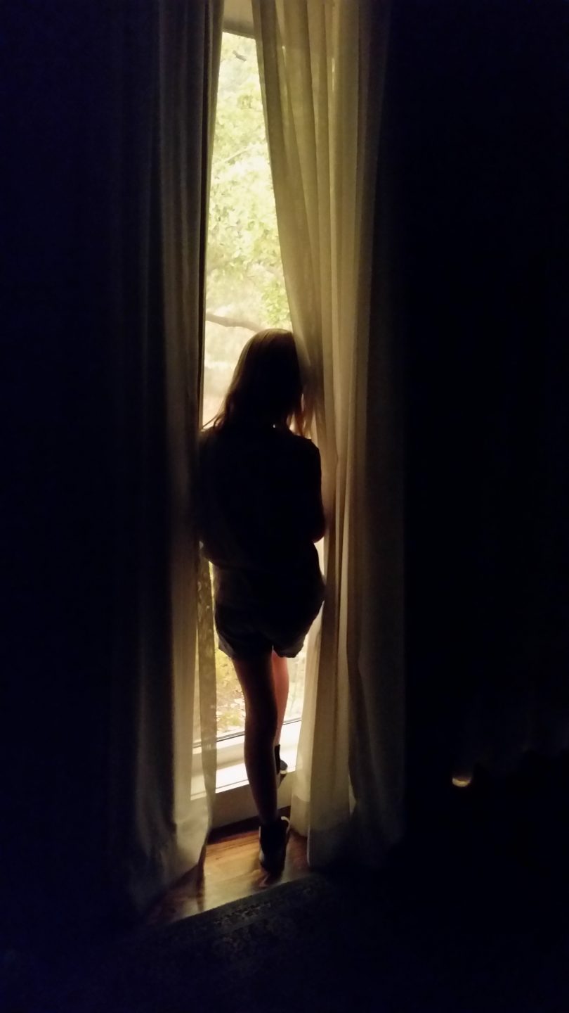 Silhouette of person standing in front of a window looking out