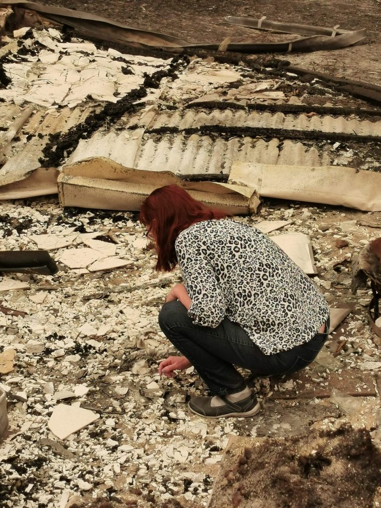 A woman squatting down over rubble from an extinguished bush fire.
