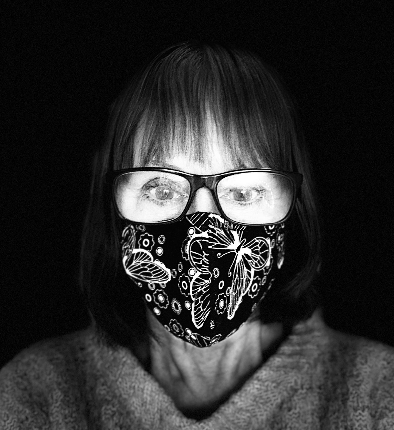 Black and white selfie of a woman wearing a glasses and a face mask. 