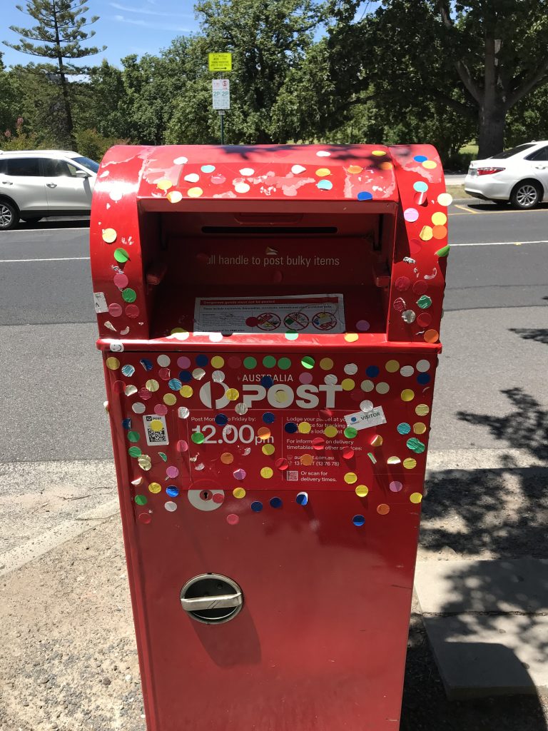 Red mail box from the front covered in coloured stick on dots.