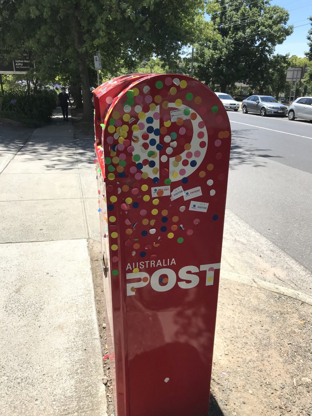 Red mail box from the side covered in coloured stick on dots.