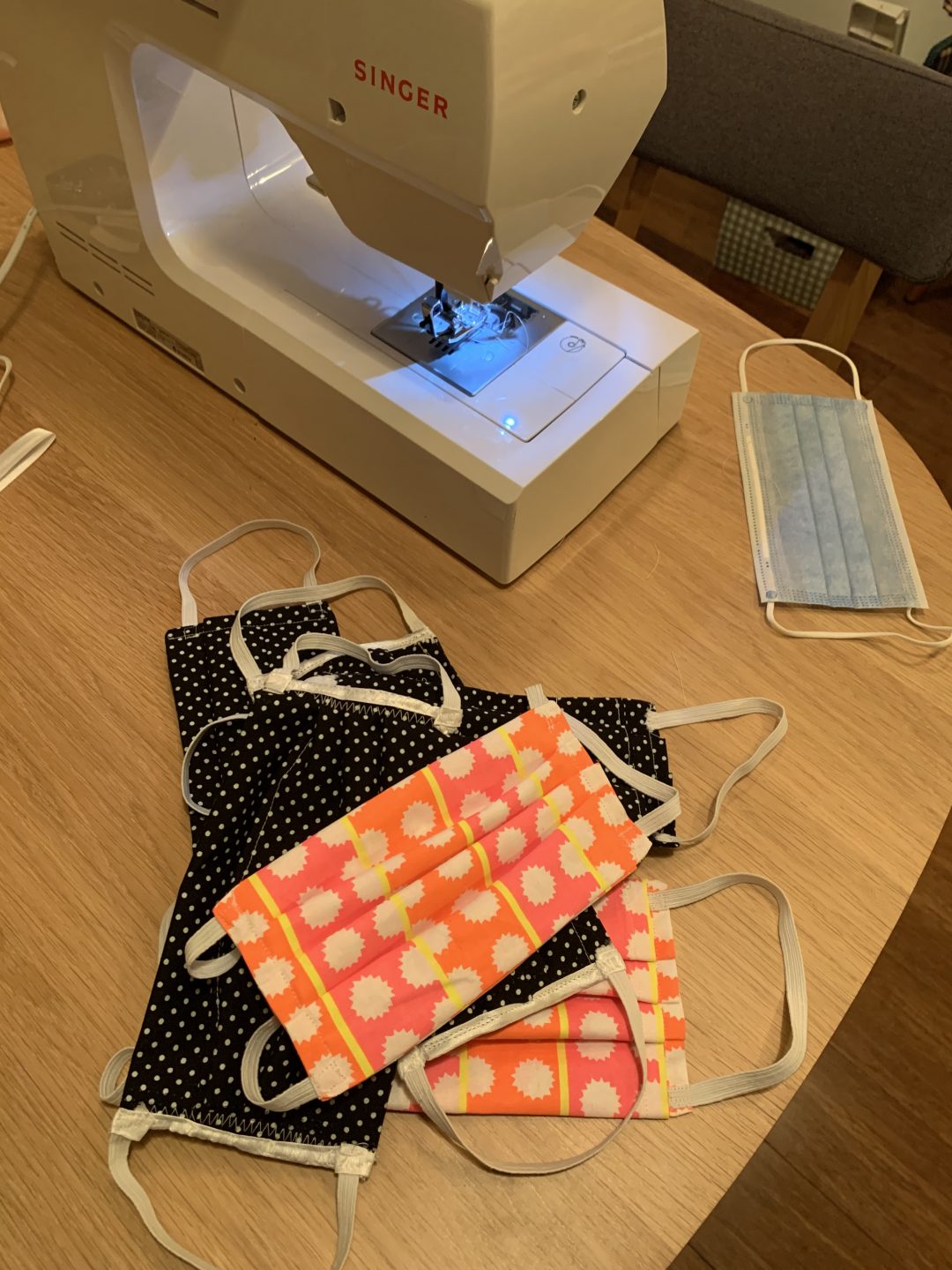 six fabric masks on a table next to a sewing machine.