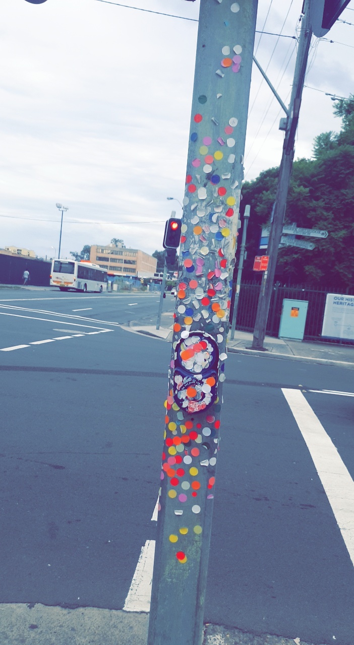 Traffic light pedestrian crossing button covered in round coloured stickers