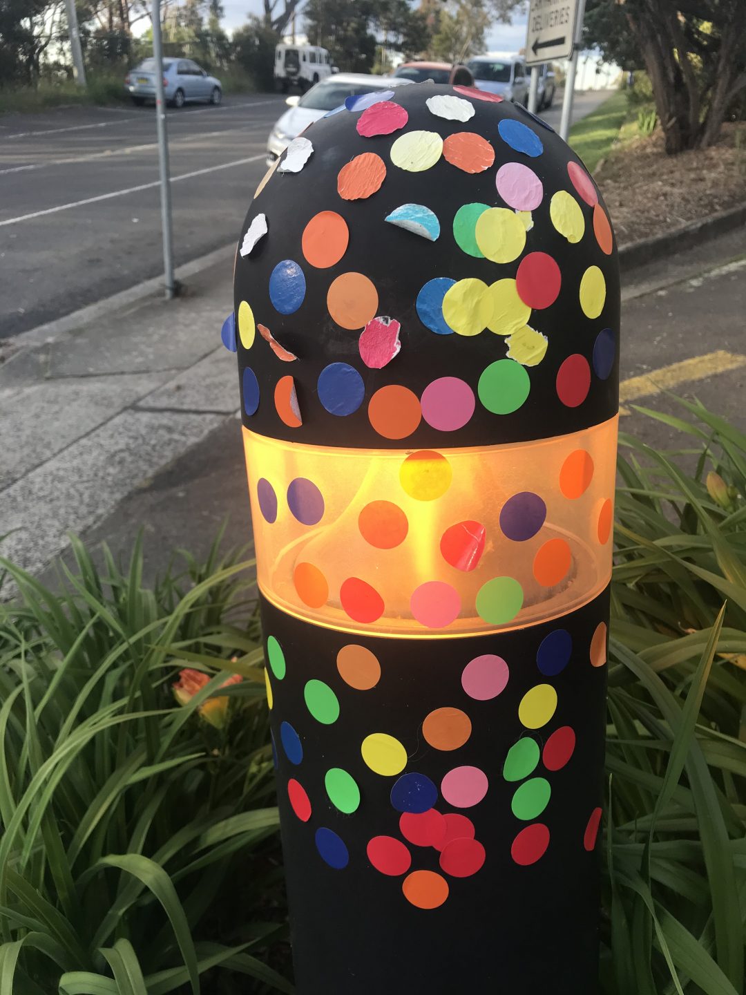 A bollard covered in coloured stickers.