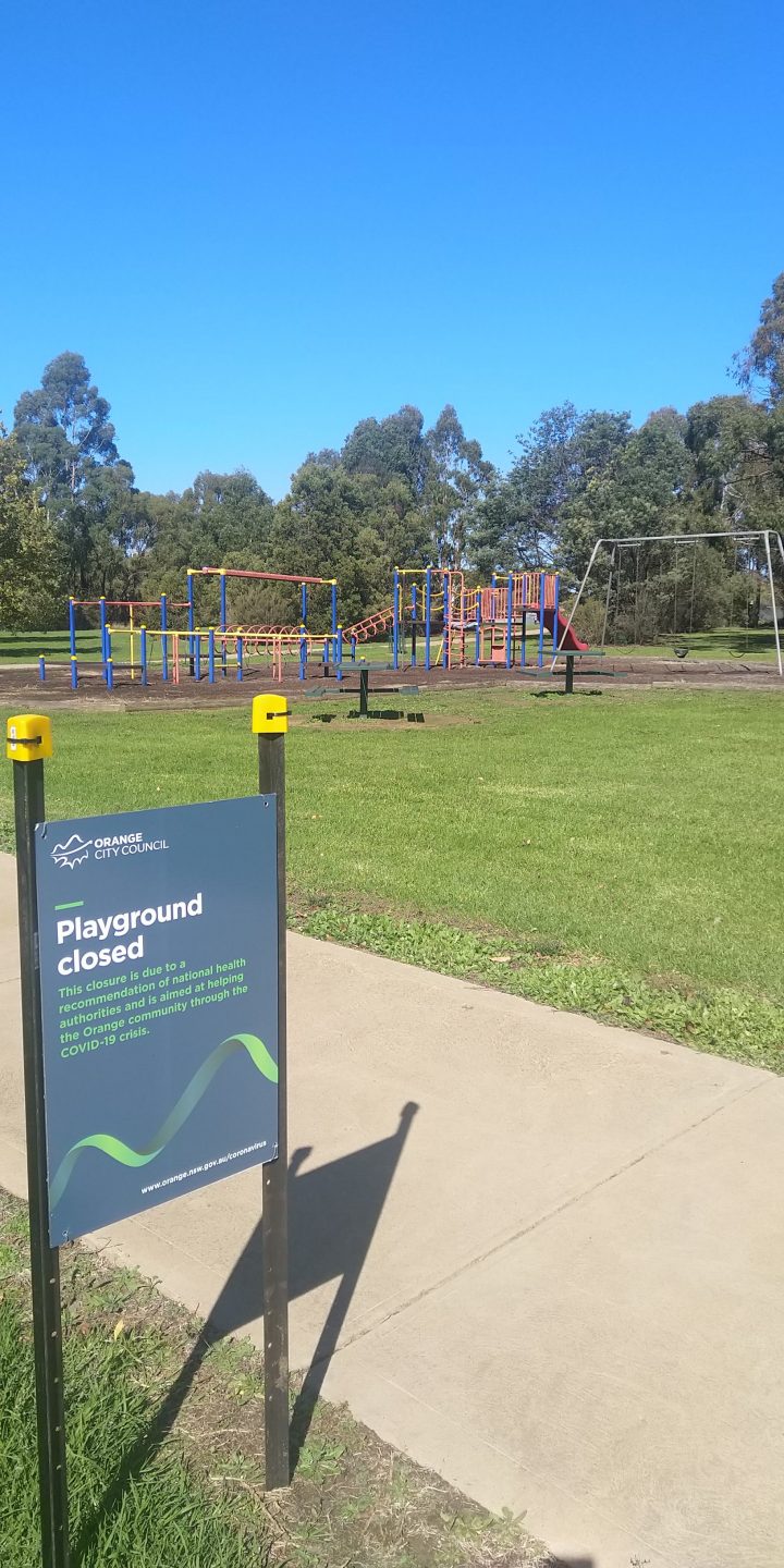 A sign that says 'playground closed' and an empty playground behind it.