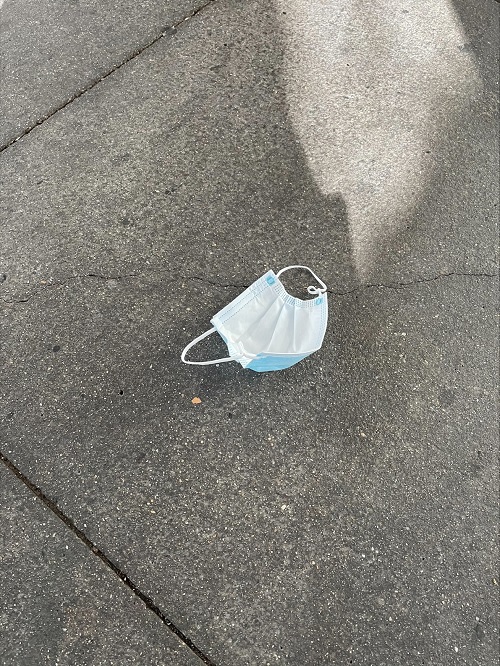 An upside down blue and white surgical mask on a grey concrete pavement