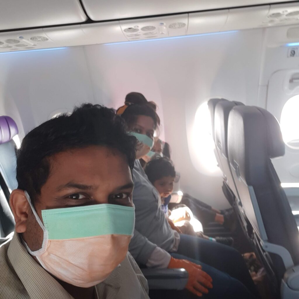 A man in a mask on an aeroplane with his family in the background also in masks.