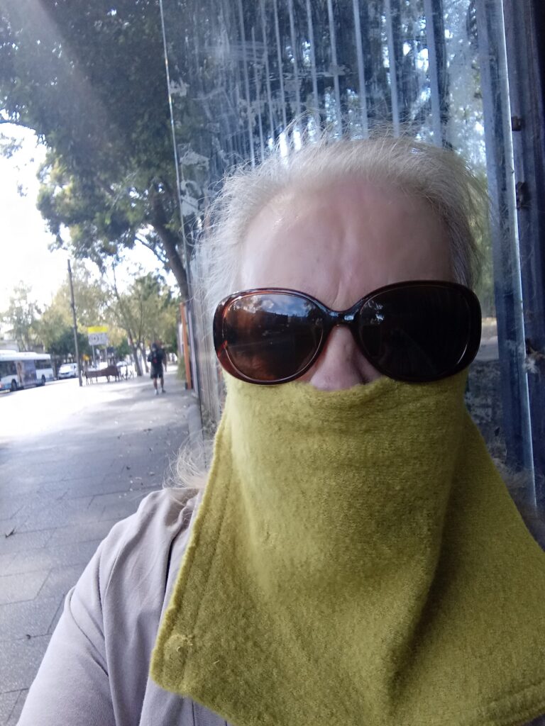 A woman with grey hair and sunglasses wearing a hand made mask.
