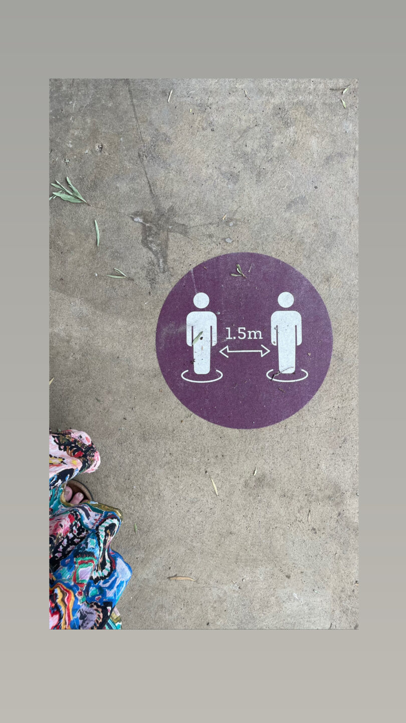 Photograph taken looking down to a concrete floor surface, with a purple circular vinyl sticker showing two white figures with 1.5m distance between then 