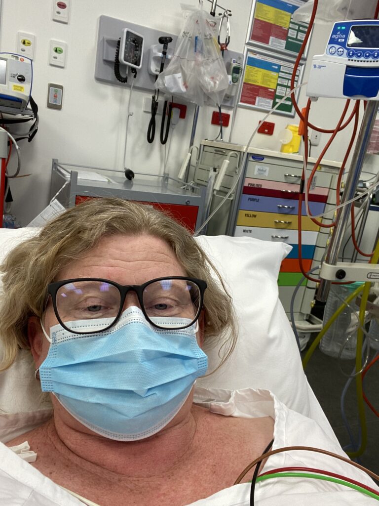 A women with blonde hair and glasses in a medical mask in a hospital bed