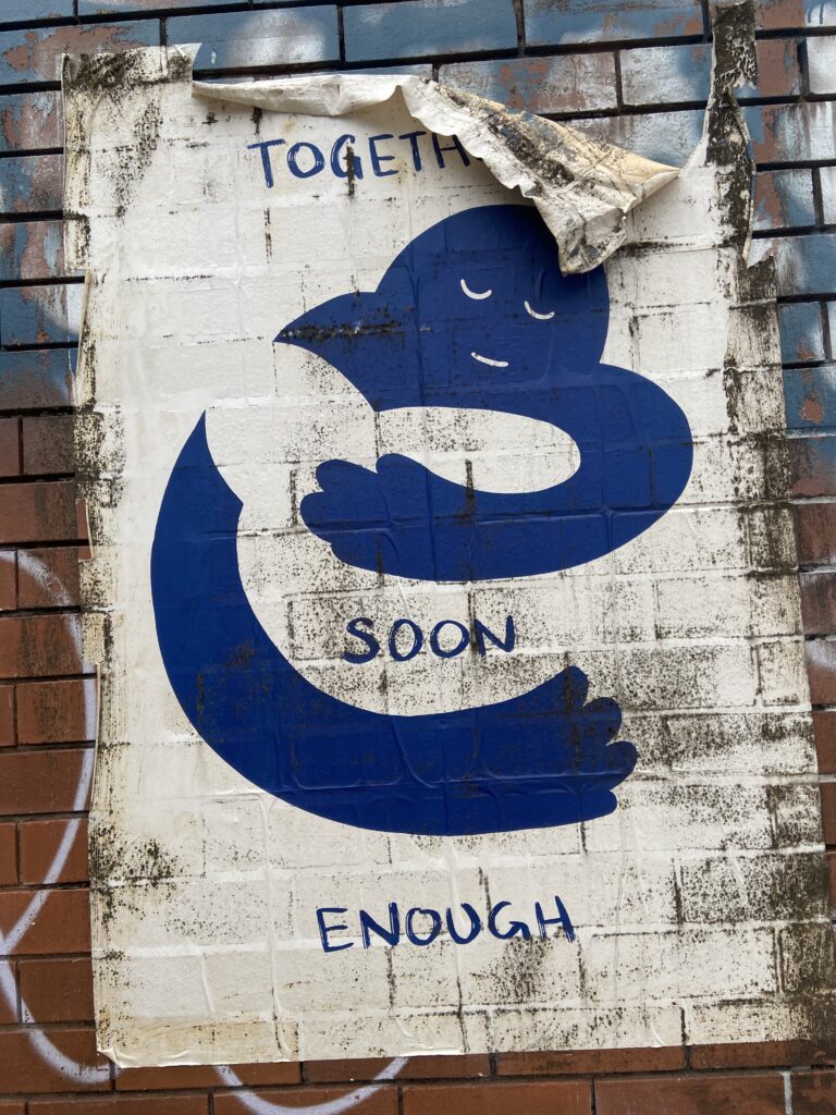 A paste up poster that says 'together soon enough' with blue and white abstract figures embracing each other.