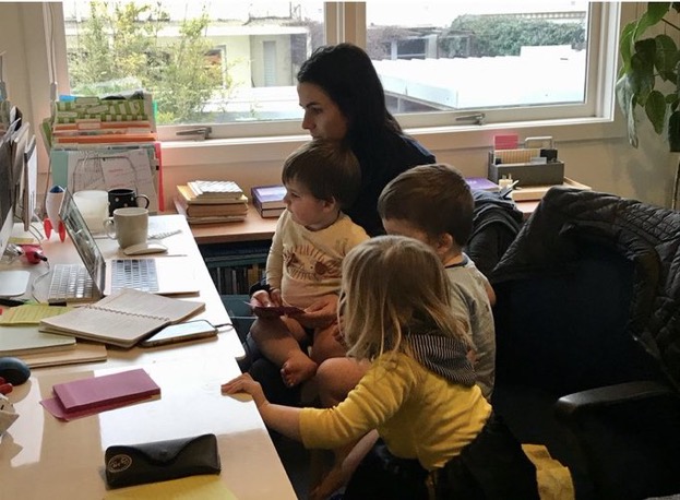 A parent working from home cuddling their three children at their work desk.