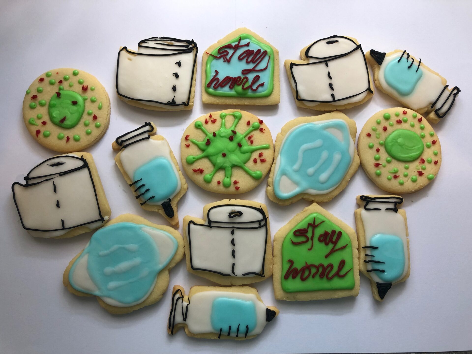 White background with 15 home-made biscuits with Covid-19 themed decoration with white, blue, green icing with red black and brown detailing. Toilet paper, the virus form, syringes and vaccine vials, as well as 'Stay Home' messaging.  - toilet 
