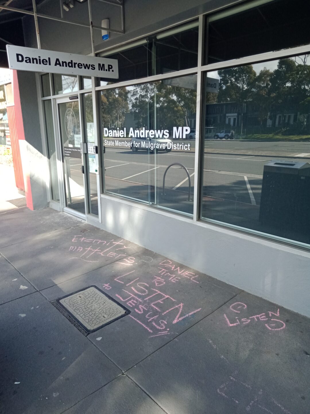 A photo of an office building with chalk drawings on the ground in pink chalk.