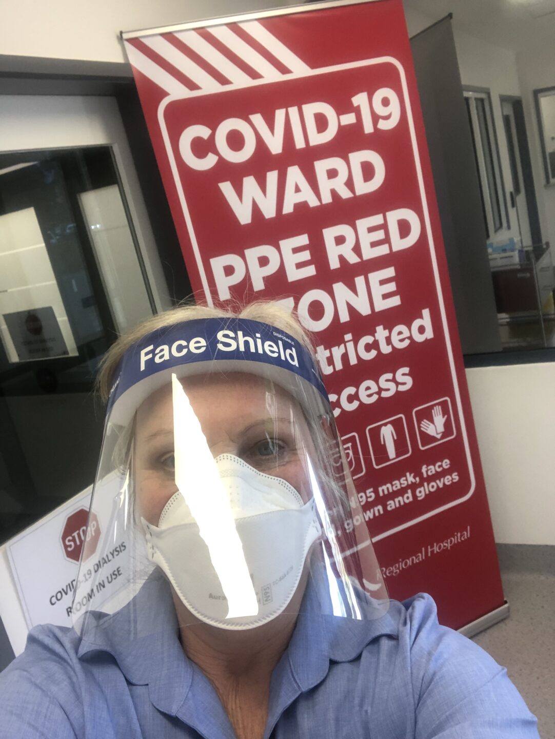 A photo of a nurse in full PPE in front of a red sign that says 'COVID-19 WARD PPE RED ZONE'