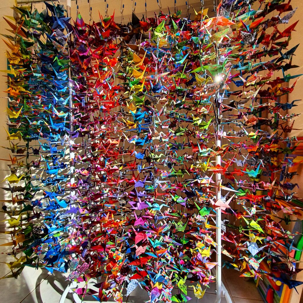 1000 colourful paper cranes handing from a ceiling in strands to the ground