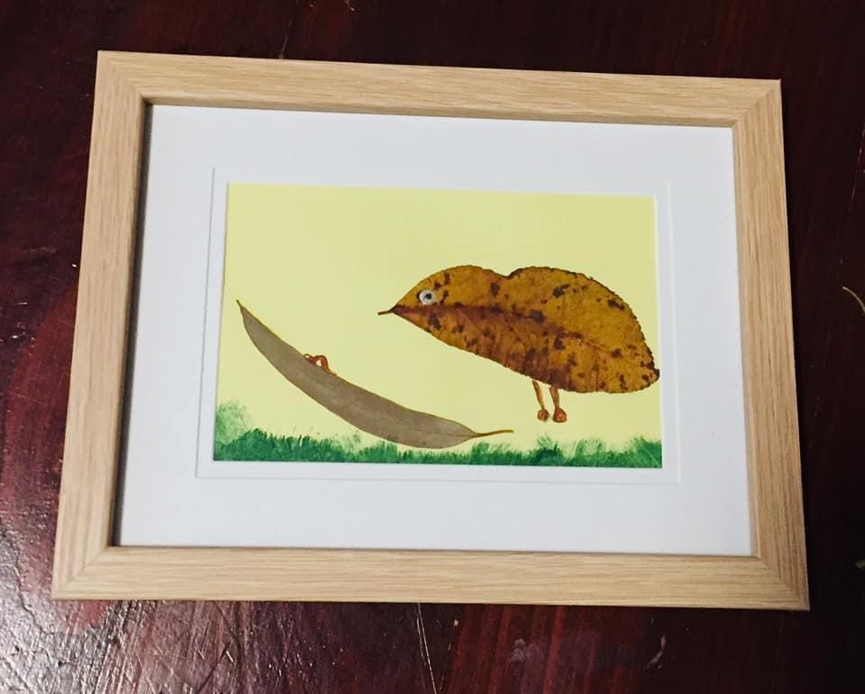 an artwork created using leaves depicting a bird flying over a figure in a hammock