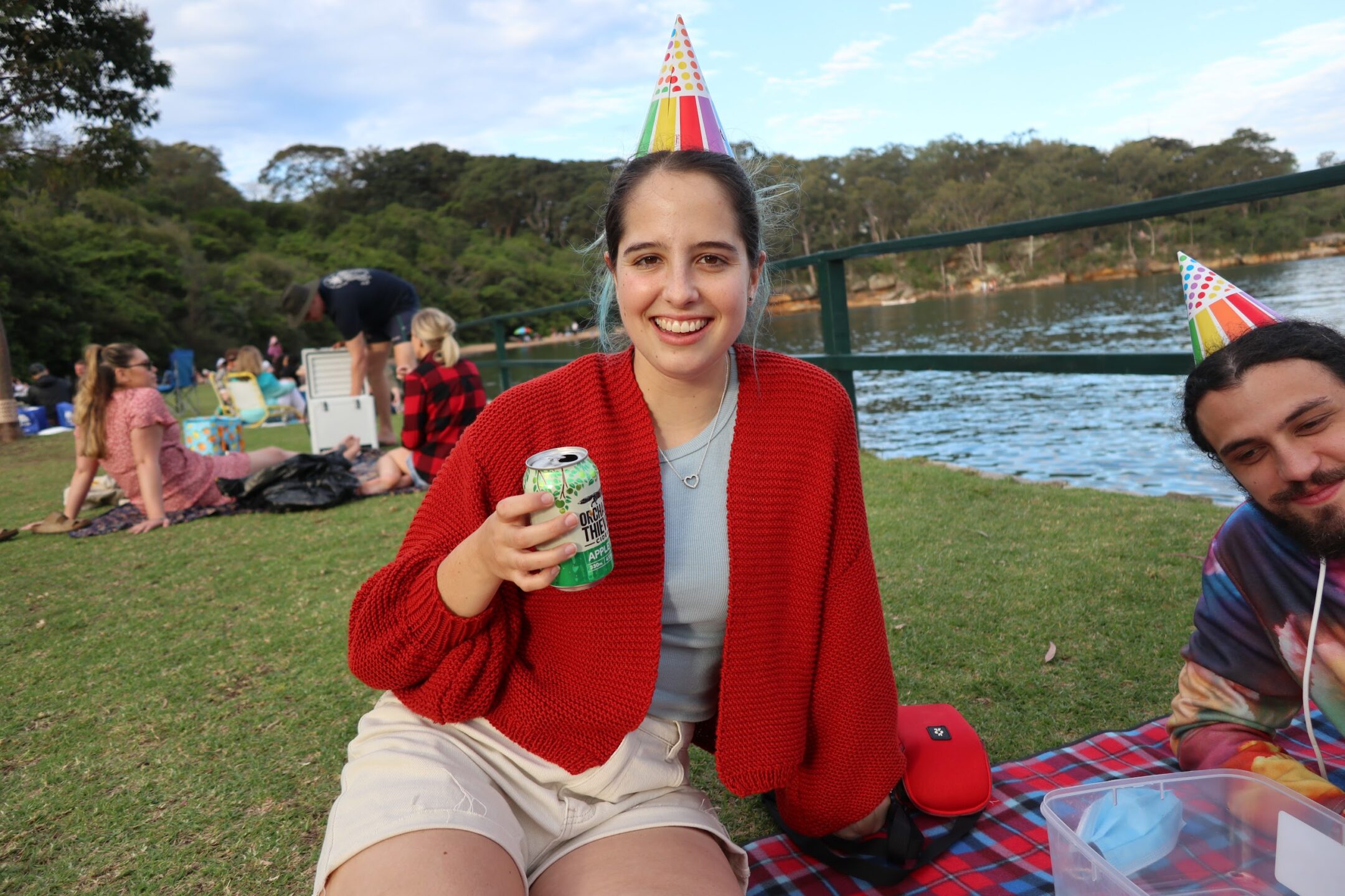 two people in colourful party hats one is in a red cardigan and holding a can of drink