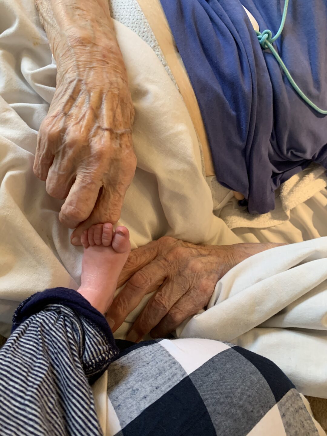A close up of an An elderly Caucasian woman's hand next to a small Caucasian baby's foot.