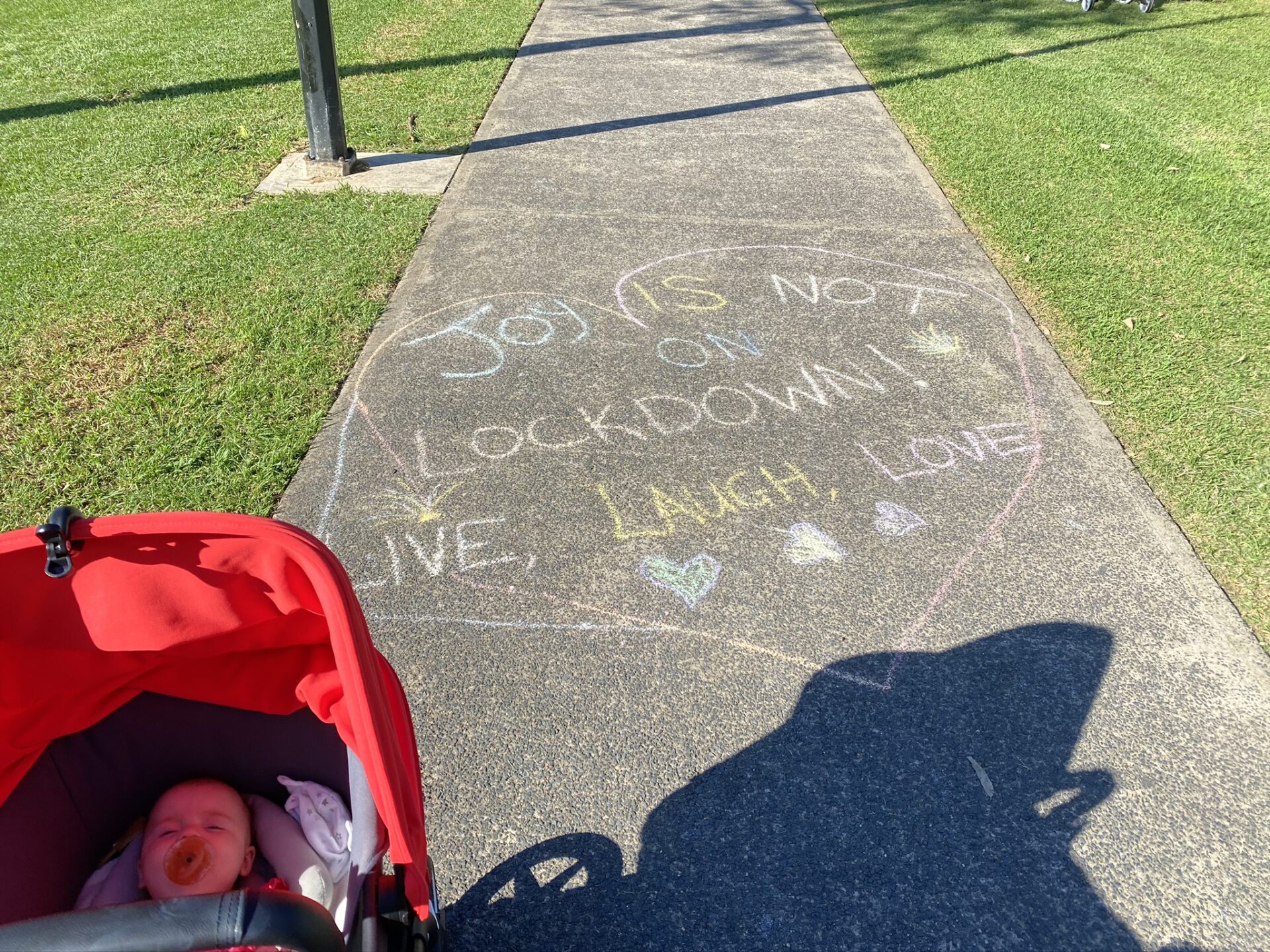 A photo of a chalk drawing on a footpath. one the pavement is written 'joy is not in lock down. Live. Laugh. Love.'