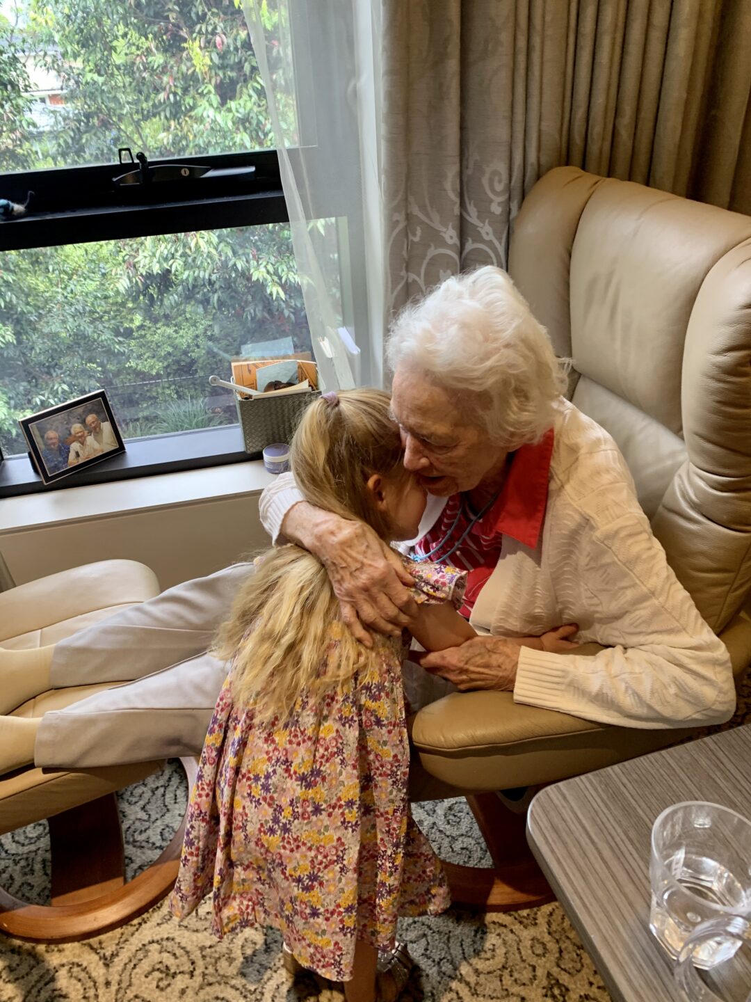 An elderly Caucasian woman with white hair hugging a small Caucasian girl with long blonde hair.