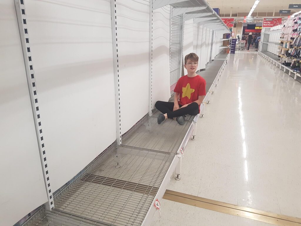 a young boy in a red t-shirt with a yellow star image on the front sitting on empty supermarket shelves