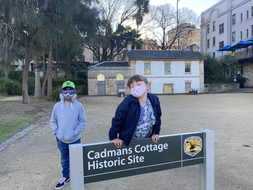 Two young children in masks in front of an historic landmark in Sydney.