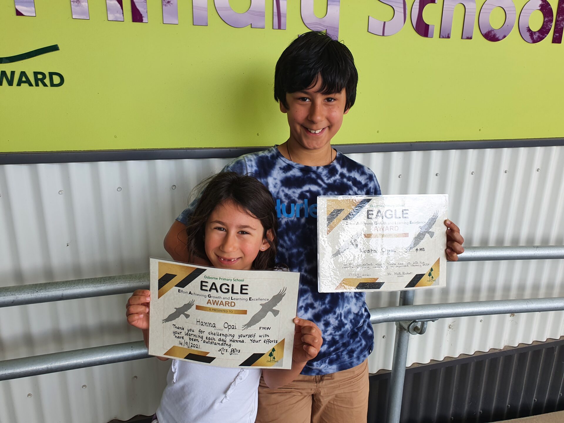 A brother and sister with dark brown hair and caucasian skin holding certificates
