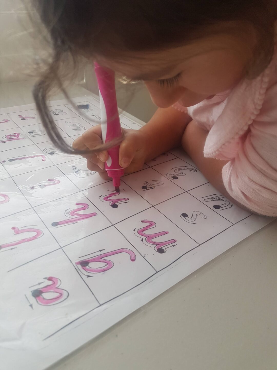 a young girl with dark brown hair and caucasian skin writing with a pink texta