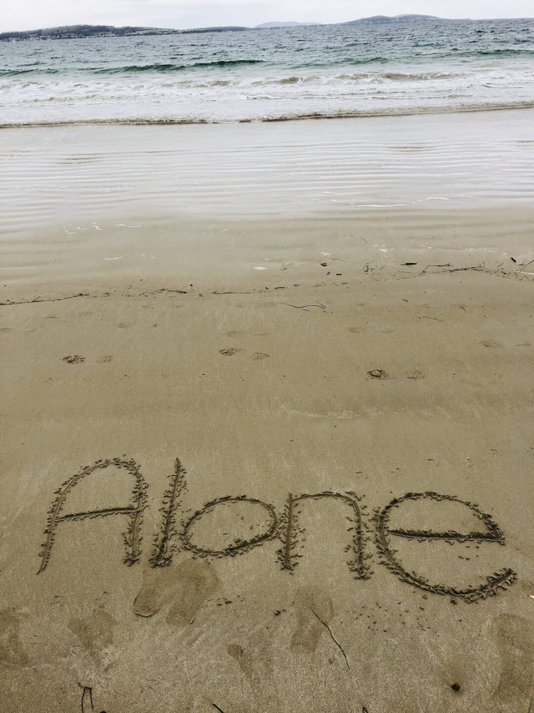 The word 'alone' written into the sand at a beach